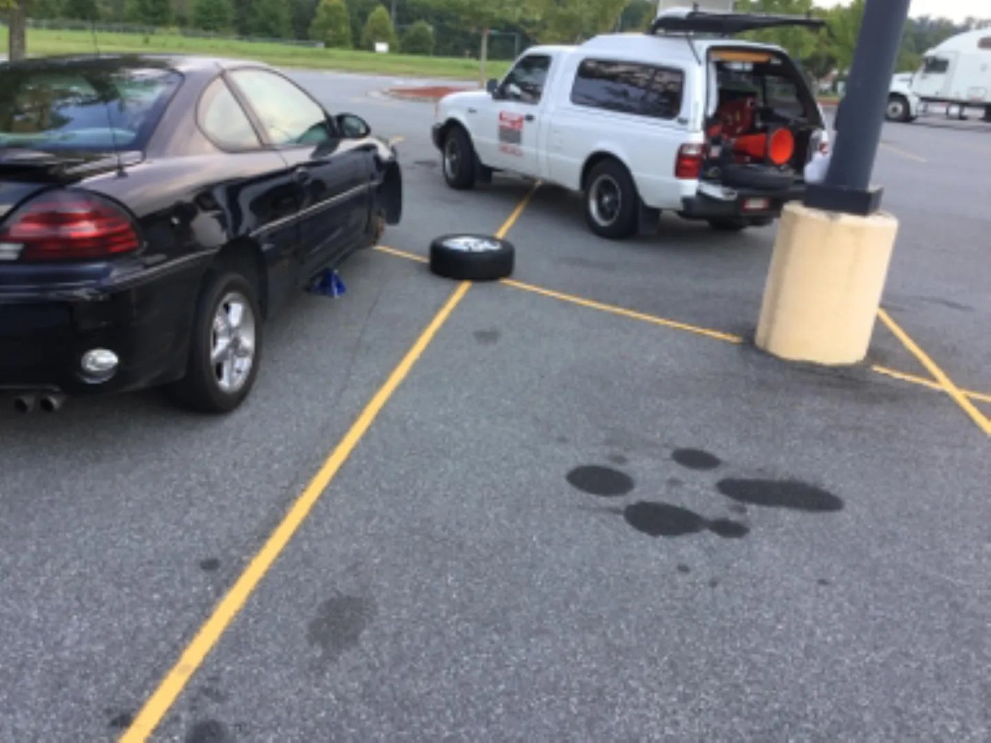 A wheel removed from a car during a mobile tire repair in a parking lot.
