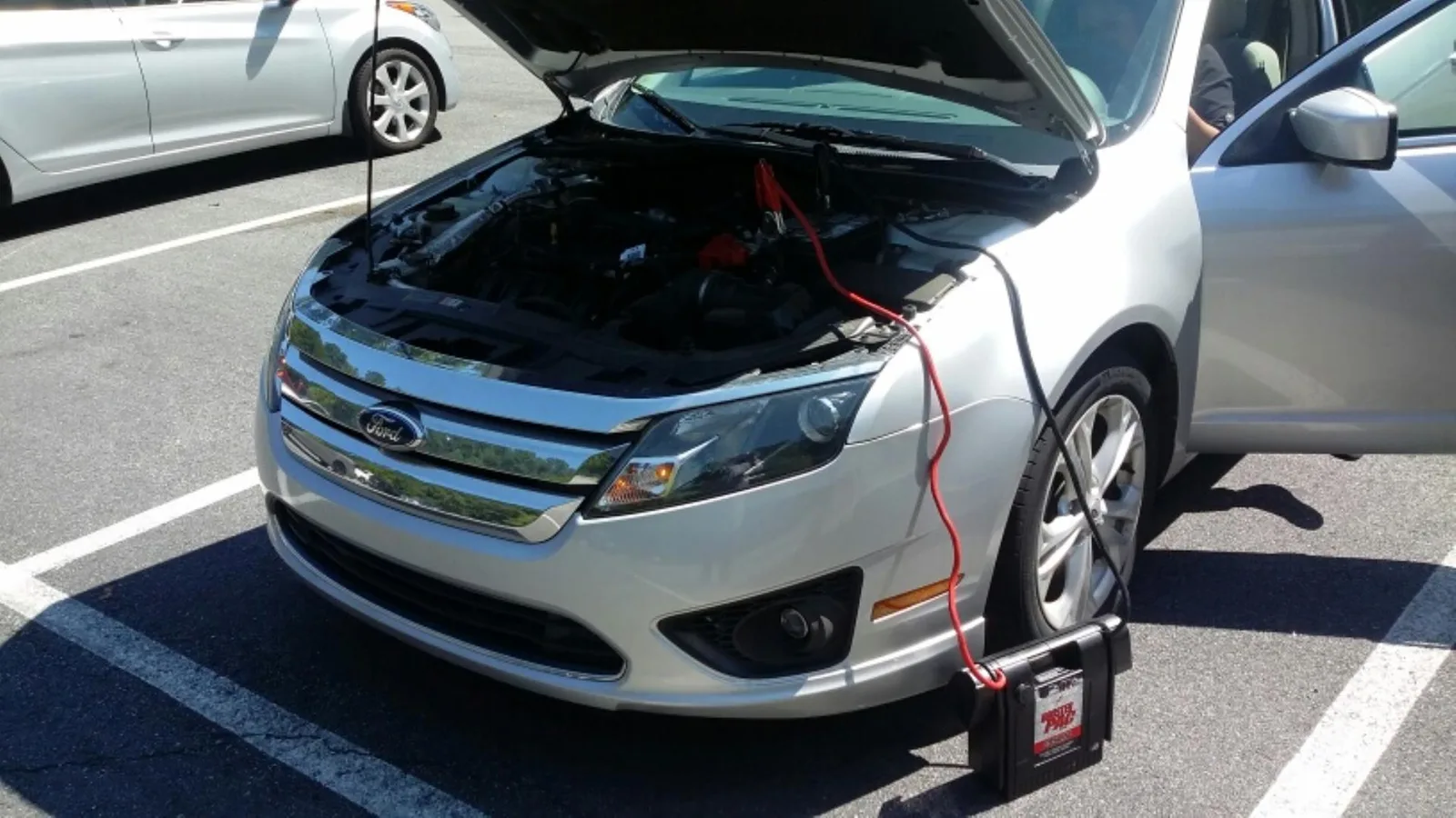 A technician jump starting a car with the hood raised.